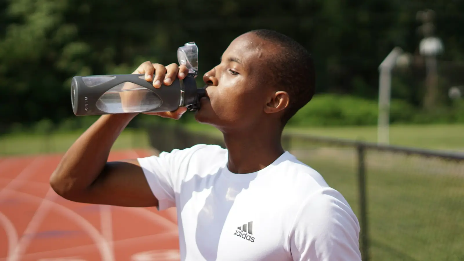 A man drinking water from a sports bottle at a running track