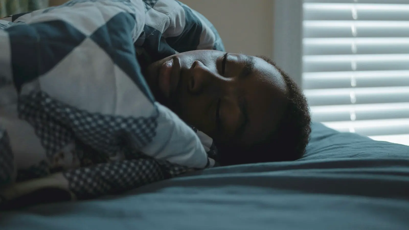 A man sleeping peacefully in bed under a patterned blanket