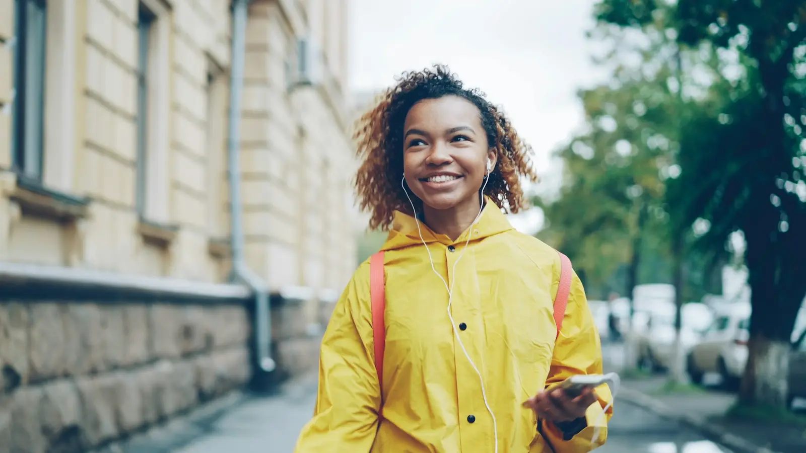 A young woman in a yellow coat walking with headphones