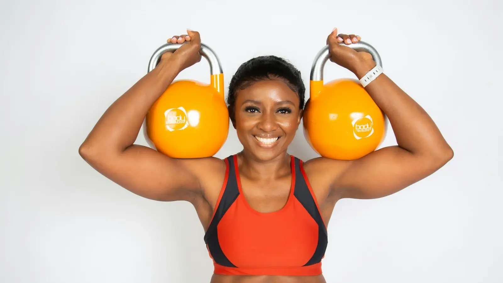 A smiling woman holding two kettlebells at shoulder height